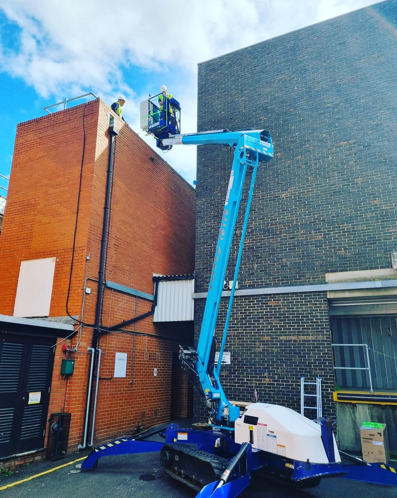 Screenshot 2026-10-07 at 16.28.37 Electrical contractor using a raised access platform beside a commercial building